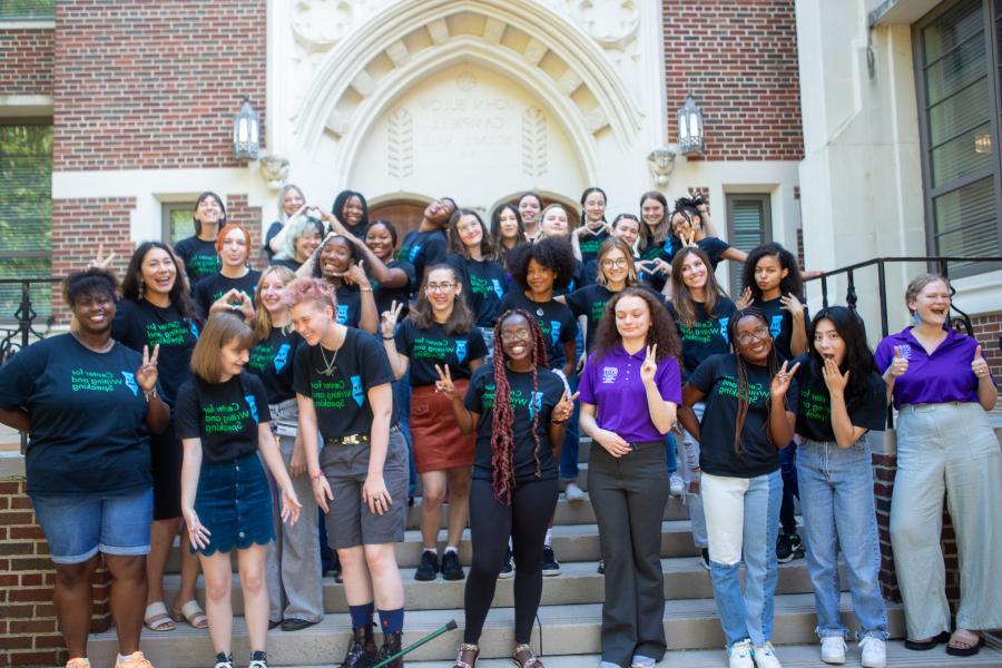 a group of student tutors gather on building stairs wearing the same branded black tee shirts